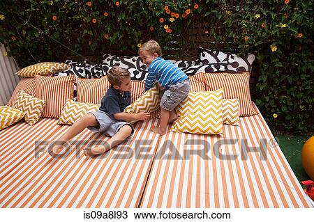 Stock Image - Two boys playing on outdoor furniture with cushions. Fotosearch