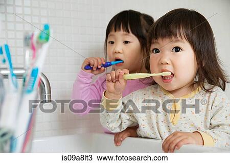 Stock Image - Two girl toddlers brushing teeth at bathroom sink. Fotosearch