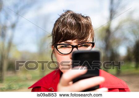 Stock Image - Woman in city park looking at smartphone. Fotosearch