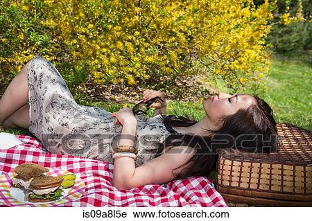 Stock Image - Woman lying on picnic blanket resting head on basket. Fotosearch