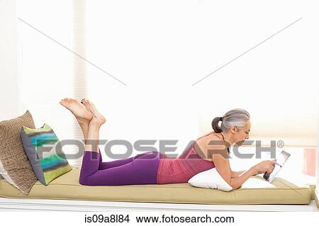 Woman lying on window seat drinking using digital tablet View Large Photo Image Picture - Woman lying on window seat drinking using digital tablet. Fotosearch