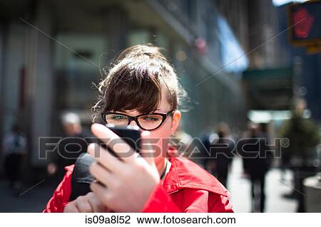 Stock Image - Woman on city street looking at smartphone. Fotosearch