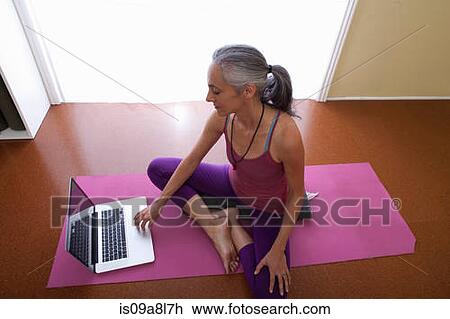 Stock Image - Woman on yoga mat, using laptop. Fotosearch