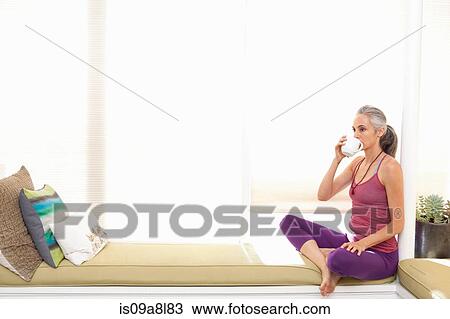 Stock Image - Woman sitting on window seat drinking herbal tea. Fotosearch