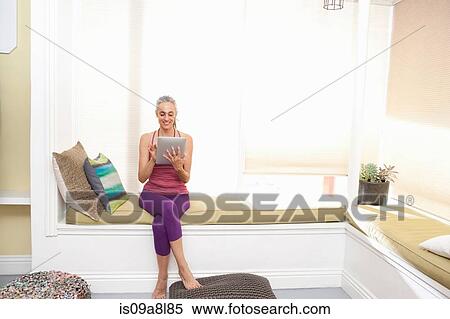 Woman sitting on window seat drinking using digital tablet View Large Photo Image Stock Photography - Woman sitting on window seat drinking using digital tablet. Fotosearch