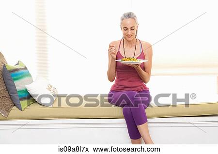 Stock Photo - Woman sitting on window seat eating lunch. Fotosearch