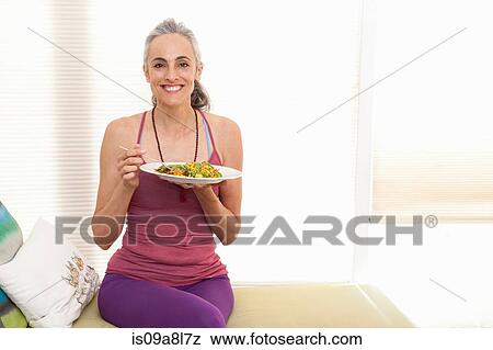 Stock Photo - Woman sitting on window seat eating lunch, portrait. Fotosearch