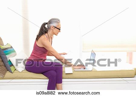 Woman sitting on window seat using laptop View Large Photo Image Stock Image - Woman sitting on window seat using laptop. Fotosearch