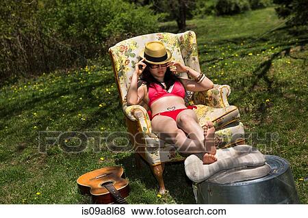 Stock Photo - Woman wearing bikini sitting in armchair in garden. Fotosearch