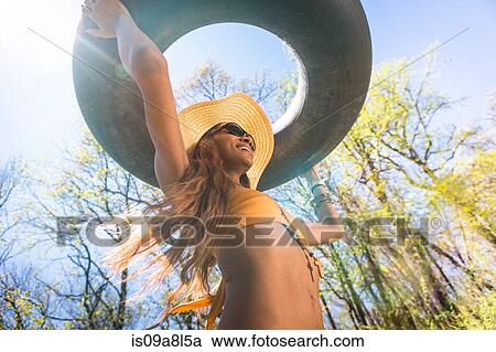 Woman wearing hat and sunglasses carrying inner tube above head View Large Photo Image Stock Image - Woman wearing hat and sunglasses carrying inner tube above head. Fotosearch