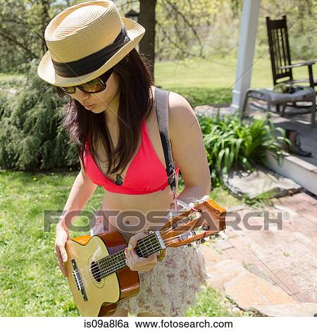 Stock Image - Woman wearing hat playing guitar. Fotosearch