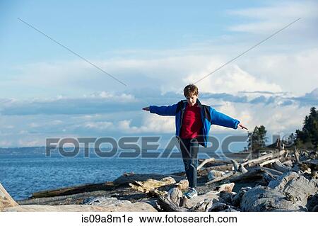 Stock Image - Young boy balancing on tree trunk at coast. Fotosearch