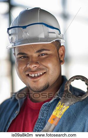 Picture - Young construction worker wearing hard hat and holding wrench, smiling. Fotosearch