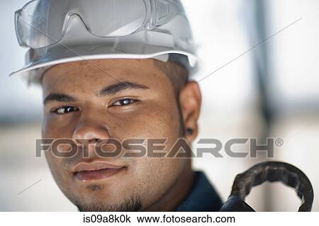 Young construction worker wearing hard hat and holding wrench, smiling View Large Photo Image Stock Image - Young construction worker wearing hard hat and holding wrench, smiling. Fotosearch