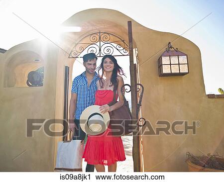 Stock Image - Young couple arriving at sunlit villa on vacation, smiling. Fotosearch