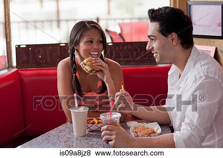 Stock Photo - Young couple eating fast food in diner. Fotosearch