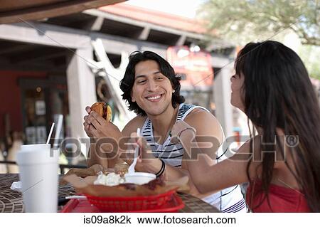 Stock Image - Young couple eating in outdoor cafe, smiling. Fotosearch