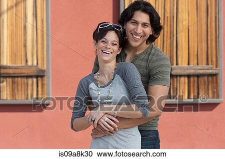 Stock Image - Young couple embracing and smiling, portrait. Fotosearch