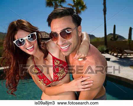 Stock Image - Young couple embracing at poolside, smiling. Fotosearch