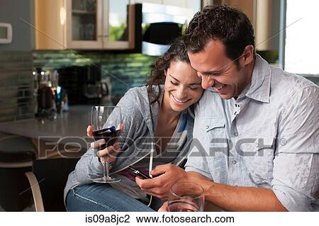 Young couple holding wine glass and looking at mobile phone View Large Photo Image Stock Image - Young couple holding wine glass and looking at mobile phone. Fotosearch