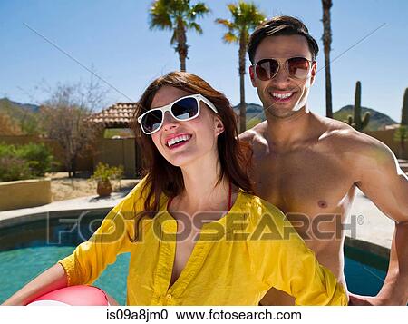 Stock Image - Young couple laughing and smiling at poolside, portrait. Fotosearch