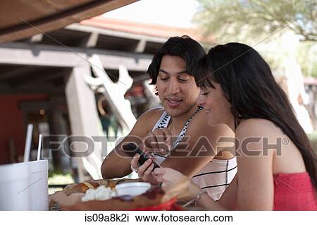 Young couple looking at mobile phone in outdoor cafe, smiling View Large Photo Image Stock Image - Young couple looking at mobile phone in outdoor cafe, smiling. Fotosearch