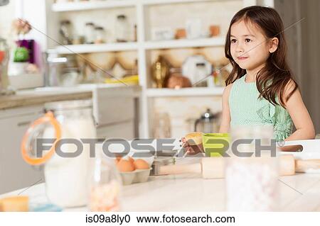 Stock Image - Young girl at kitchen counter measuring ingredients. Fotosearch