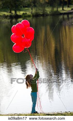 Young girl in front of lake with bunch of red balloons View Large Photo Image Stock Photo - Young girl in front of lake with bunch of red balloons. Fotosearch