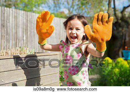 Stock Image - Young girl in garden wearing oversized gloves. Fotosearch