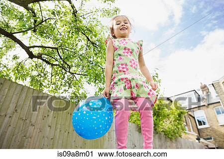 Stock Image - Young girl jumping in garden with balloon. Fotosearch