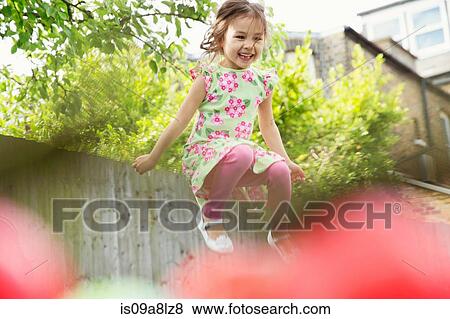 Stock Photo - Young girl jumping mid air in garden. Fotosearch