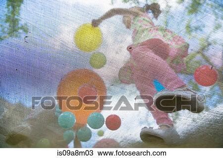 Stock Image - Young girls bouncing on garden trampoline. Fotosearch