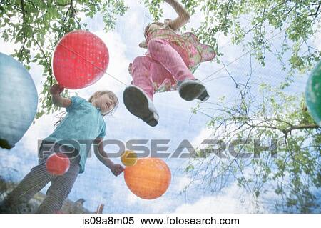 Stock Photography - Young girls jumping on garden trampoline with balloons. Fotosearch