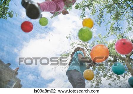 Stock Image - Young girls jumping on garden trampoline. Fotosearch