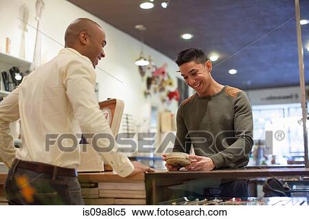 Stock Photography - Young man buying item from shopkeeper in vintage shop. Fotosearch