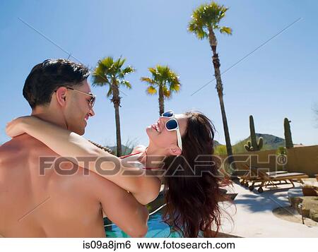 Stock Photograph - Young man carrying woman near poolside, smiling. Fotosearch