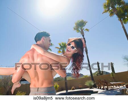 Young man carrying woman near poolside, smiling View Large Photo Image Stock Photography - Young man carrying woman near poolside, smiling. Fotosearch