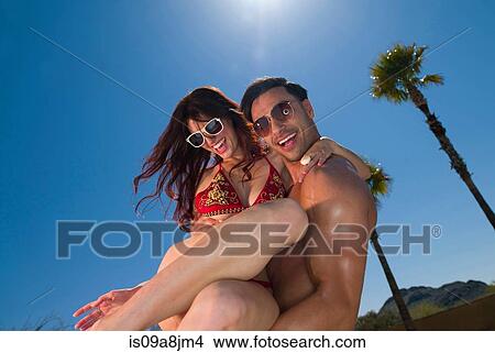 Young man carrying woman on vacation, smiling View Large Photo Image Picture - Young man carrying woman on vacation, smiling. Fotosearch