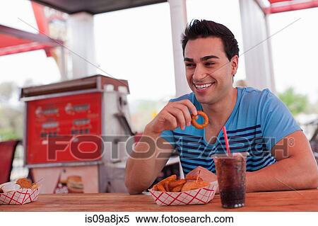 Young man eating onion rings in diner, smiling View Large Photo Image Stock Photography - Young man eating onion rings in diner, smiling. Fotosearch