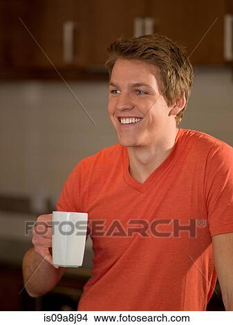 Young man holding cup of coffee in kitchen View Large Photo Image Picture - Young man holding cup of coffee in kitchen. Fotosearch