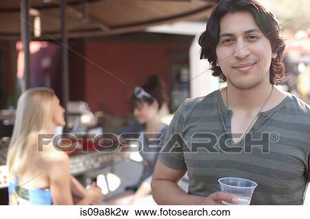 Young man holding drink and smiling in outdoor cafe, portrait View Large Photo Image Stock Photo - Young man holding drink and smiling in outdoor cafe, portrait. Fotosearch