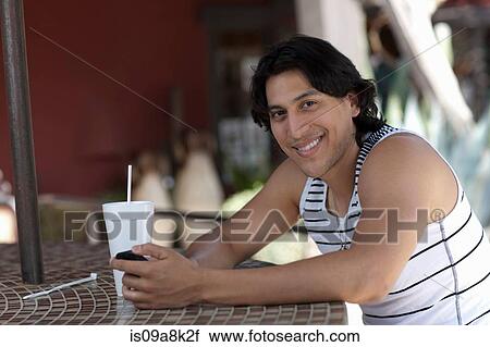 Stock Image - Young man holding mobile phone in outdoor cafe, portrait. Fotosearch