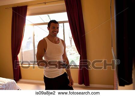 Stock Image - Young man in vest holding television remote control in hotel room. Fotosearch