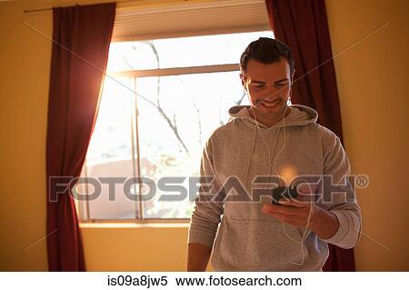 Stock Photography - Young man listening to mp3 player in hotel room, smiling. Fotosearch