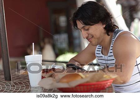 Young man looking at mobile phone in outdoor cafe, smiling View Large Photo Image Stock Image - Young man looking at mobile phone in outdoor cafe, smiling. Fotosearch