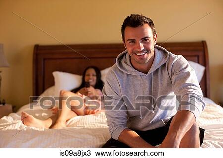 Young man sitting on bed in hotel room, smiling View Large Photo Image Stock Image - Young man sitting on bed in hotel room, smiling. Fotosearch
