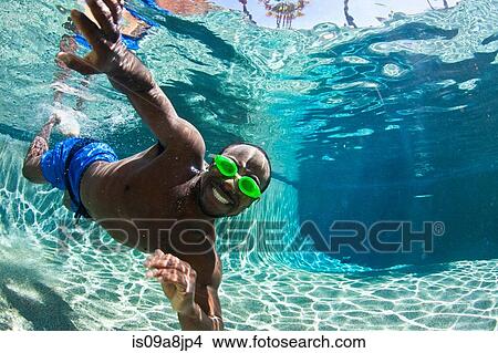 Picture - Young man swimming underwater in pool, portrait. Fotosearch