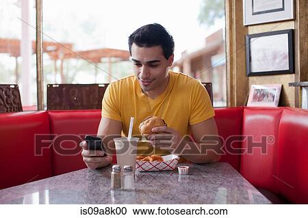 Young man texting on mobile phone and eating fast food in diner View Large Photo Image Stock Image - Young man texting on mobile phone and eating fast food in diner. Fotosearch