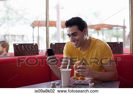 Young man texting on mobile phone and eating fast food in diner View Large Photo Image Stock Image - Young man texting on mobile phone and eating fast food in diner. Fotosearch
