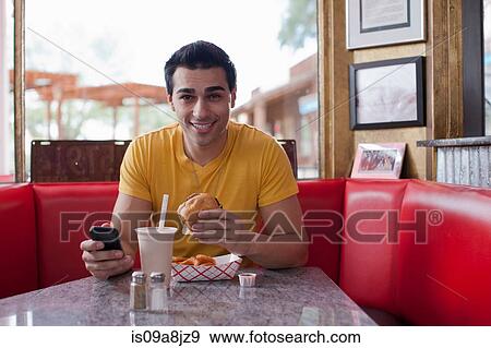 Young man texting on mobile phone and eating fast food in diner, portrait View Large Photo Image Stock Photo - Young man texting on mobile phone and eating fast food in diner, portrait. Fotosearch